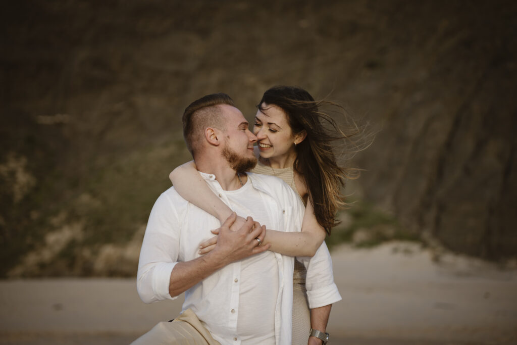 Couple smiling and embracing at the beach.
