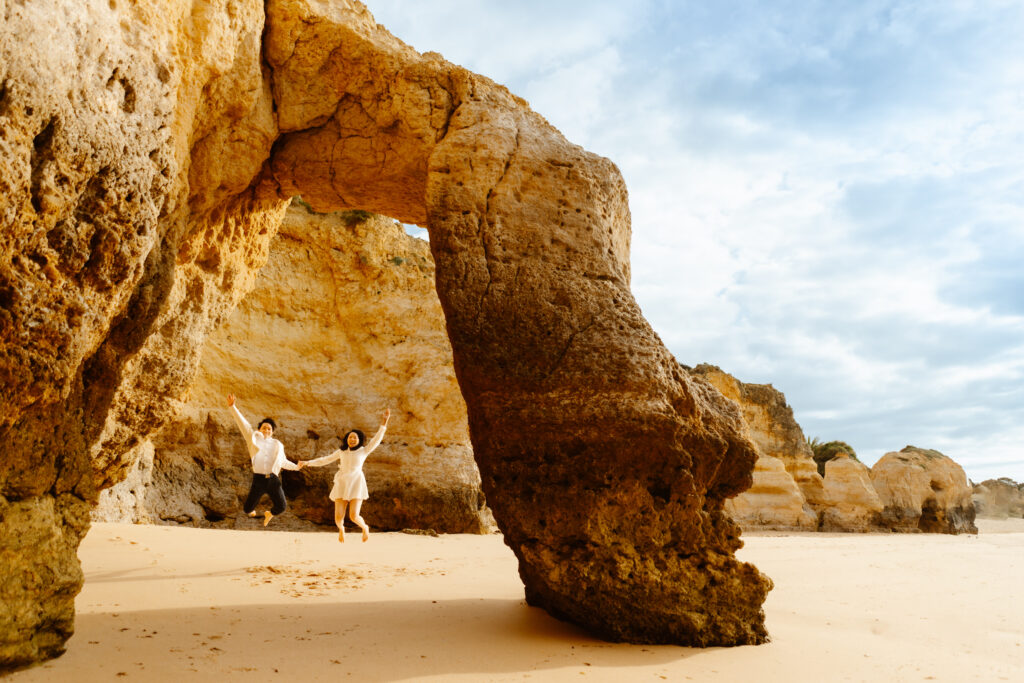 a couple jumping below arch on sao rafael beach in albufeira