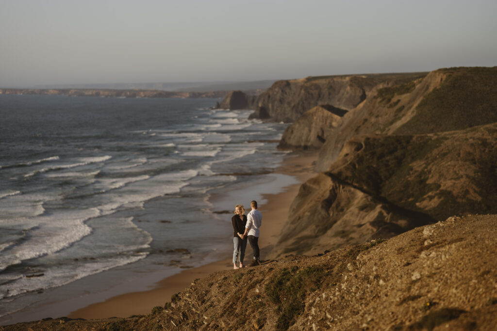 A couple holding hands at a rocky beach near the water