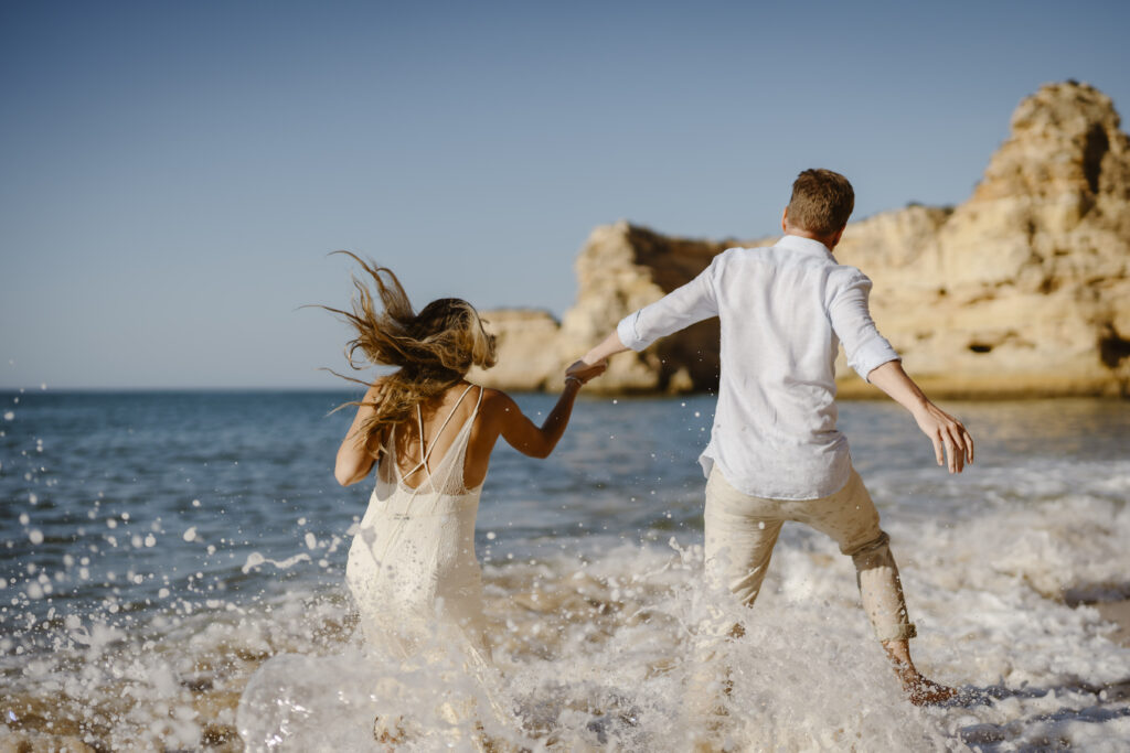 Bride and groom running through the water at the beach
