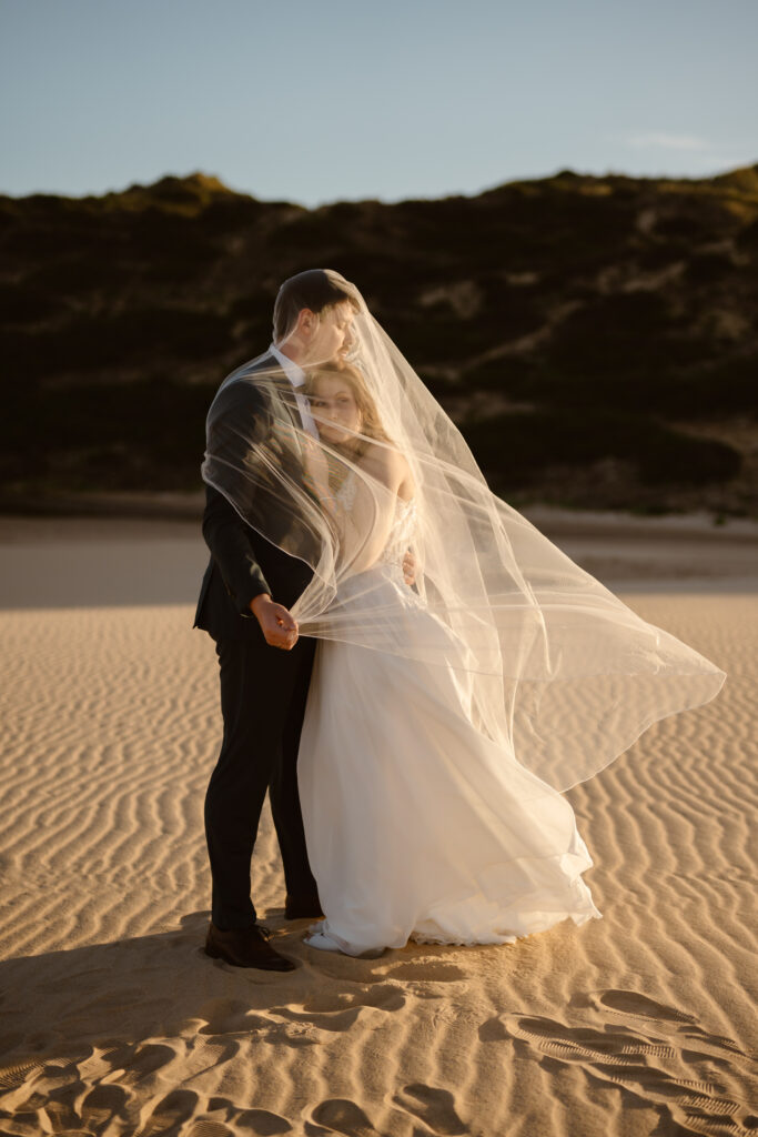 Bride and groom under the wedding veil at Bordeira beach. Elopement in west coast of Algarve.