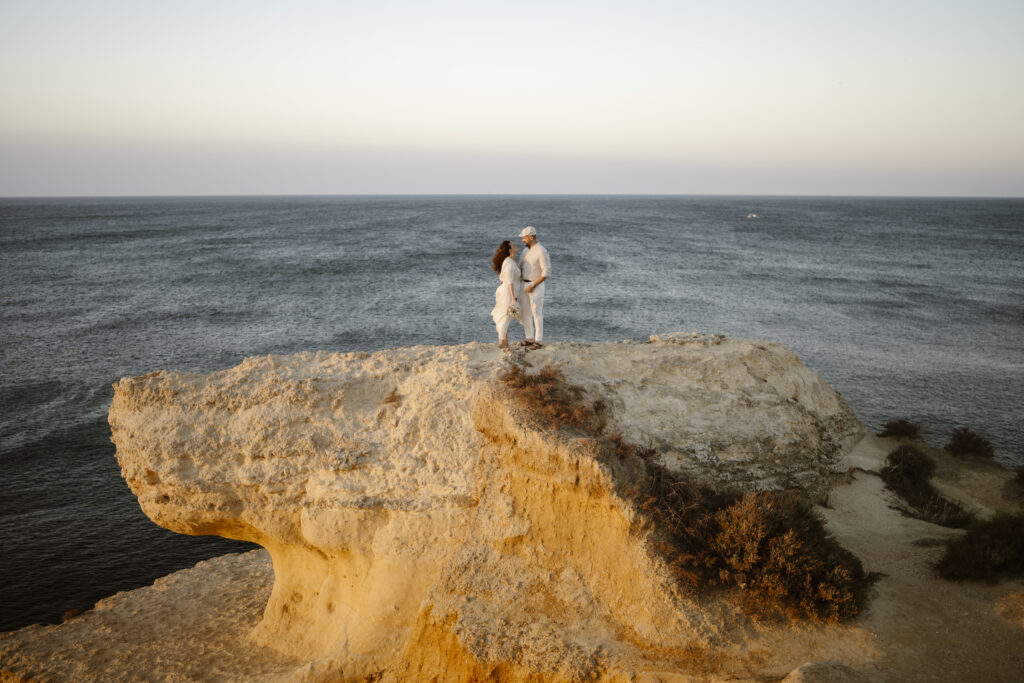 couple stand on large rock over looking the water