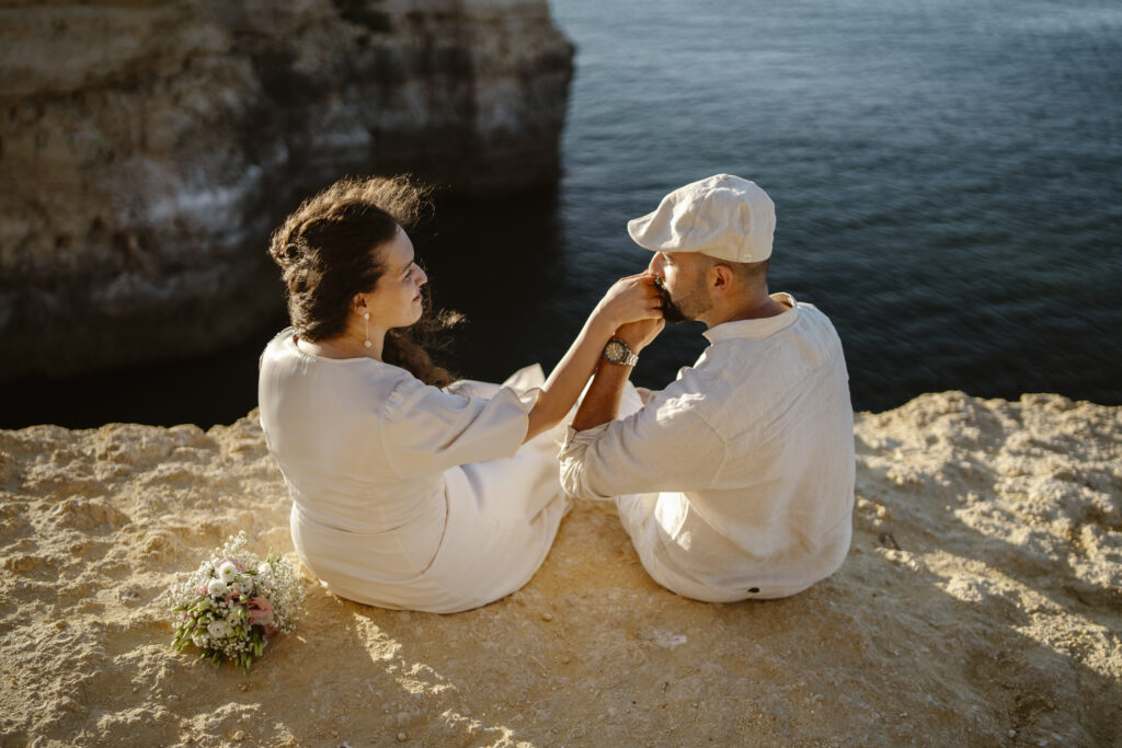 A man kisses his fiancés hand on cliff