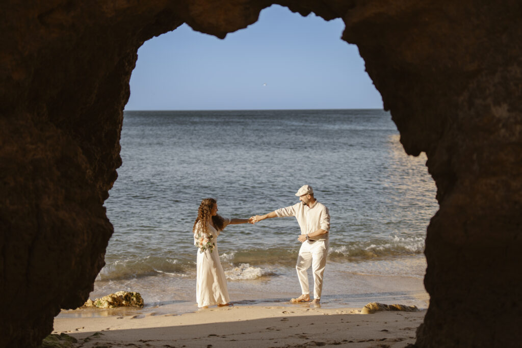 Couple hold hands at entrance of cave on the beach
