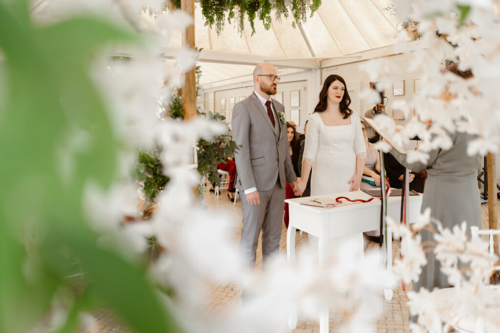 Bride and groom stand at alter surrounded by white flowers