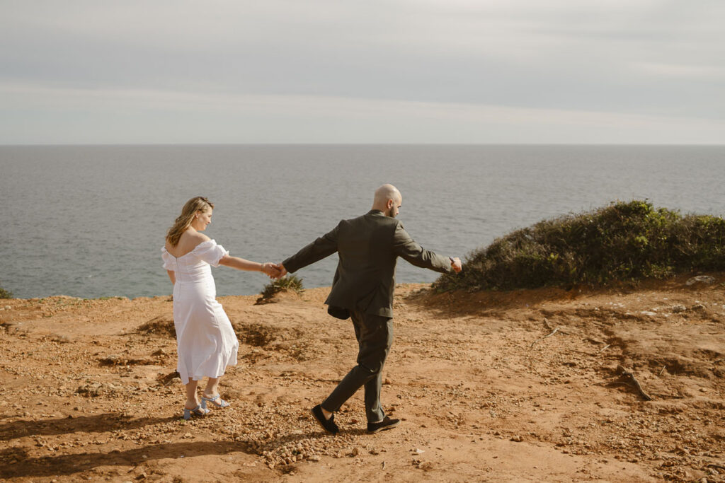 Bride and groom walk towards cliffside in Alvor, Portugal