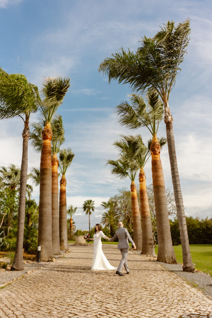 Bride and groom holding hands beneath tall palm trees