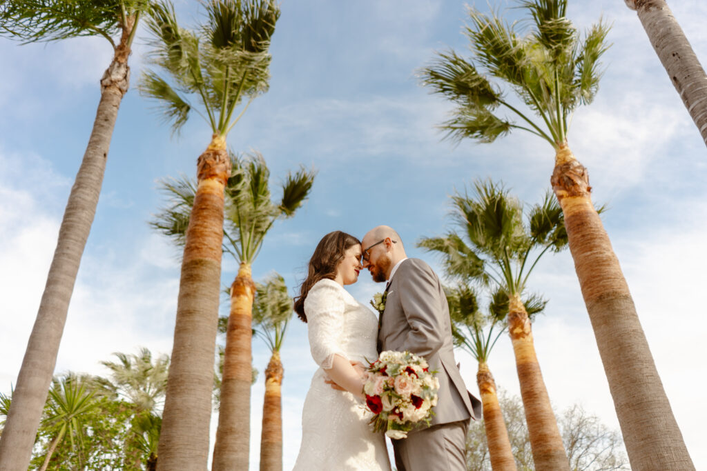 Bride and groom embrace between tall palm trees