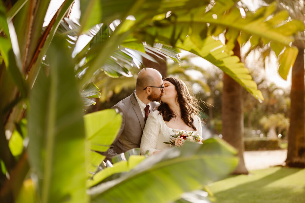Married couple kiss surrounded by palm leaves