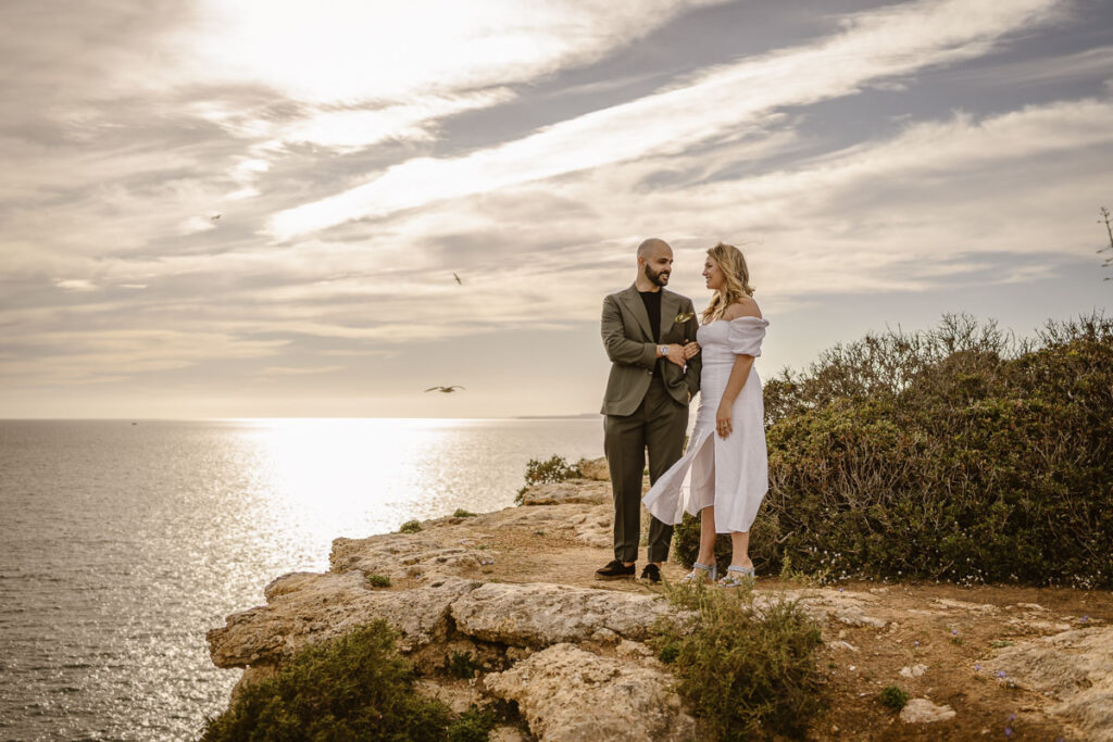 Bride and groom stood facing ocean on cliffside in Alvor, Portugal