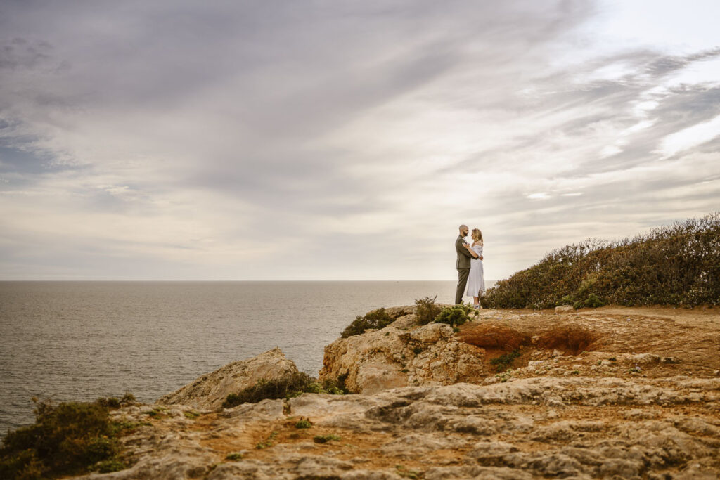 Bride and groom embrace at cliffside in Alvor, Portugal
