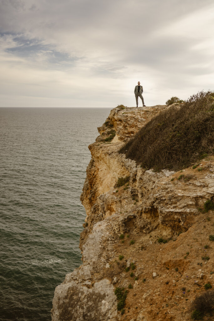 Groom stands alone at side of cliff in Alvor, Portugal
