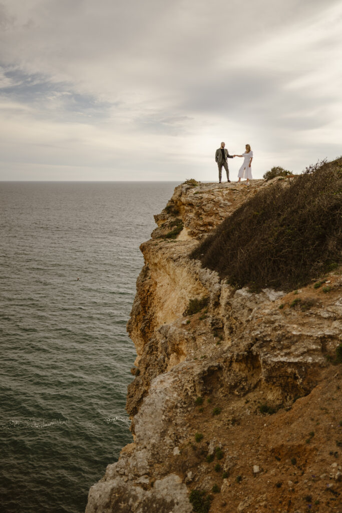 Bride and groom stand on cliffside in Alvor, Portugal