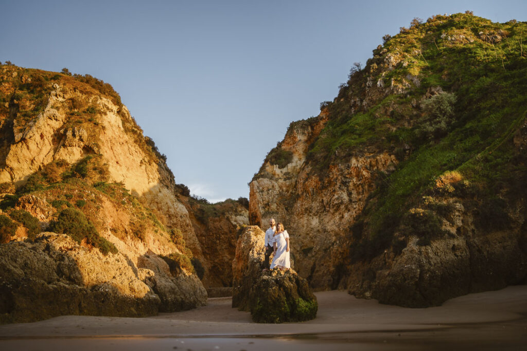 Bride and groom stand on rocks on beach in Alvor, Portugal