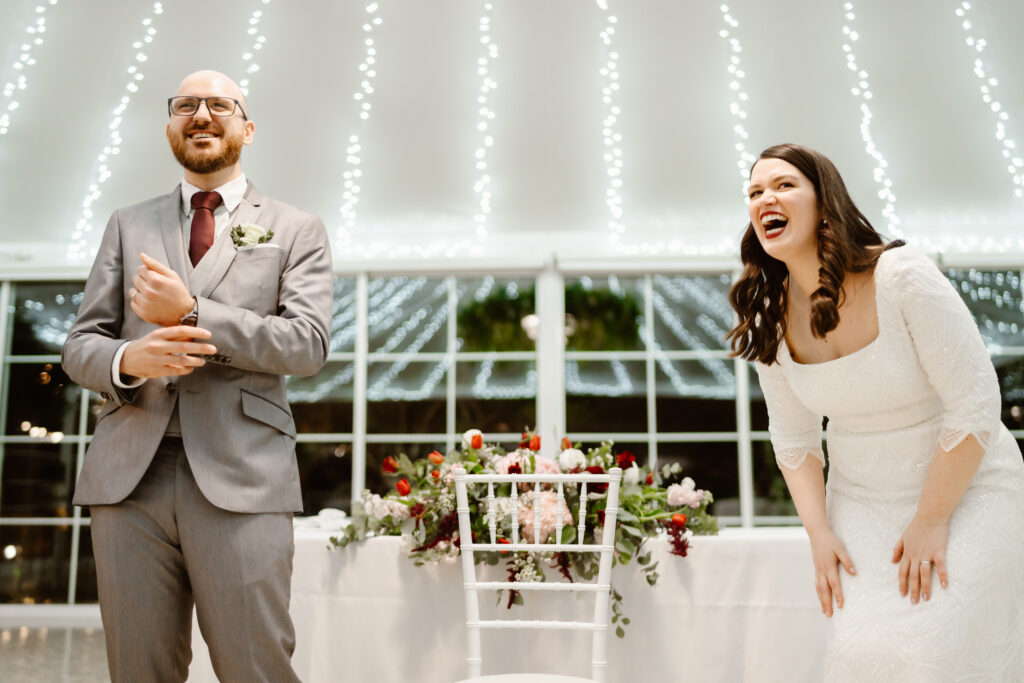 Bride and groom laughing together next to table with flowers