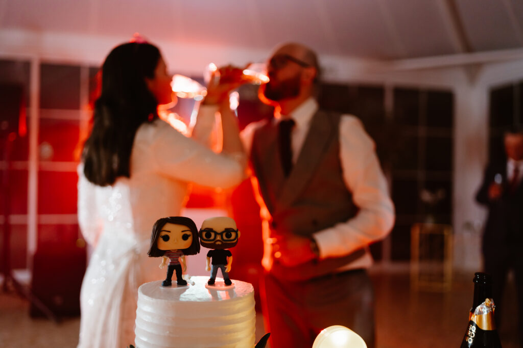 Bride and groom drink together behind wedding cake