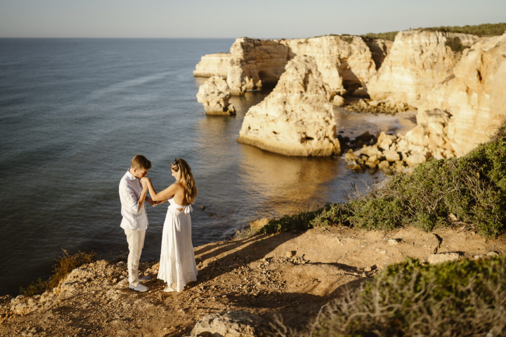 Man kisses fiancés hand on cliff