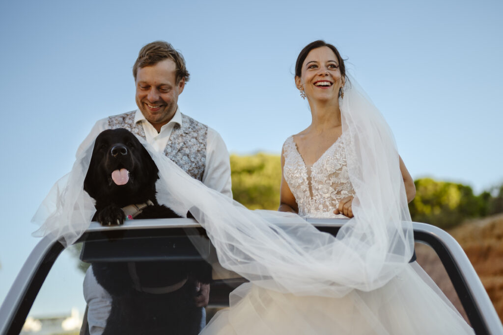 A bride and groom in a car with a dog