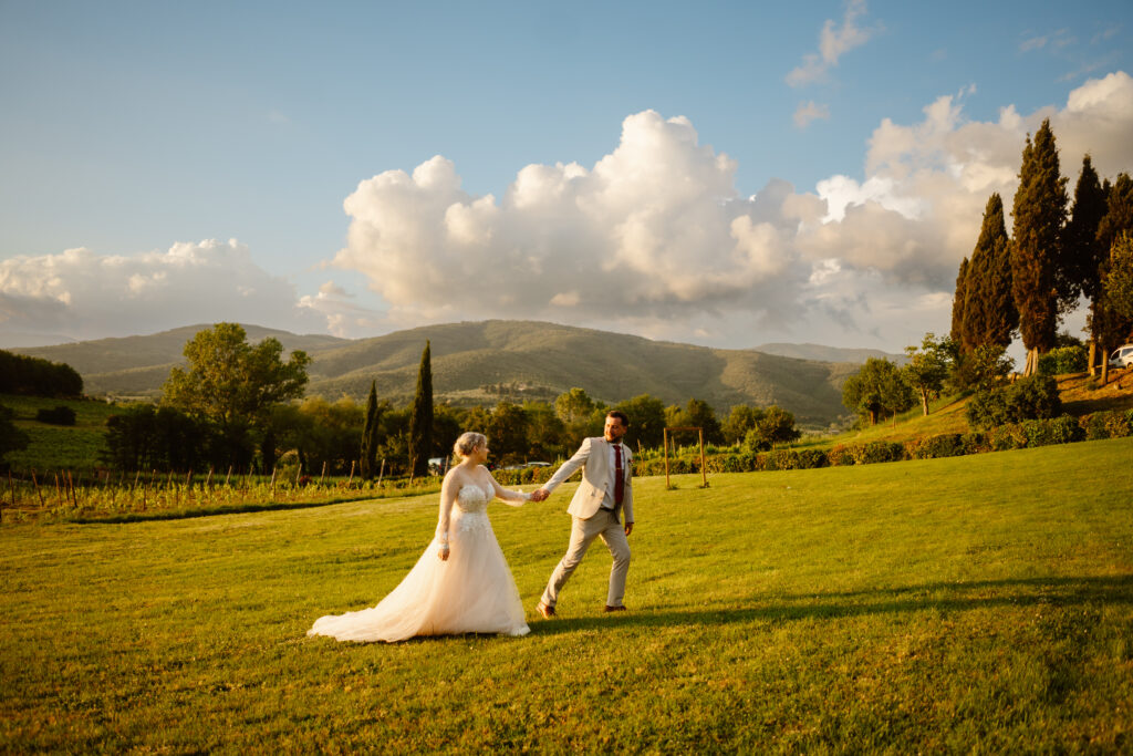 Bride and groom holding hands walking through grassy area with large hills