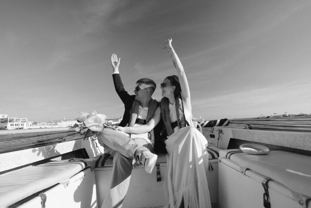Bride and groom wave on boat in Algarve, Portugal