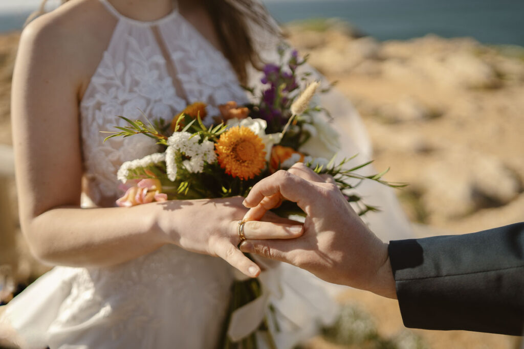 Groom places ring on brides hand in Bordeira, Portugal
