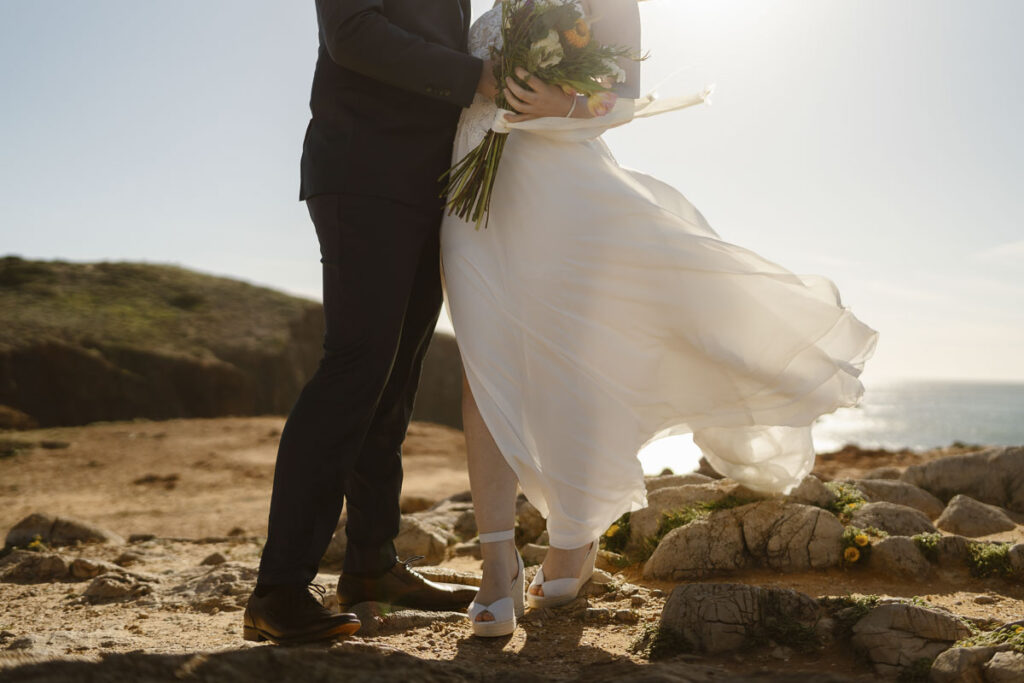 Bride and groom hold bouquet in Bordeira, Portugal