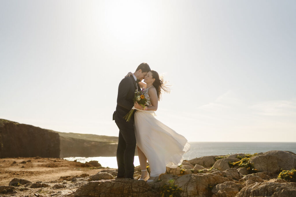 Bride hugs grooms on beach in Bordeira, Portugal