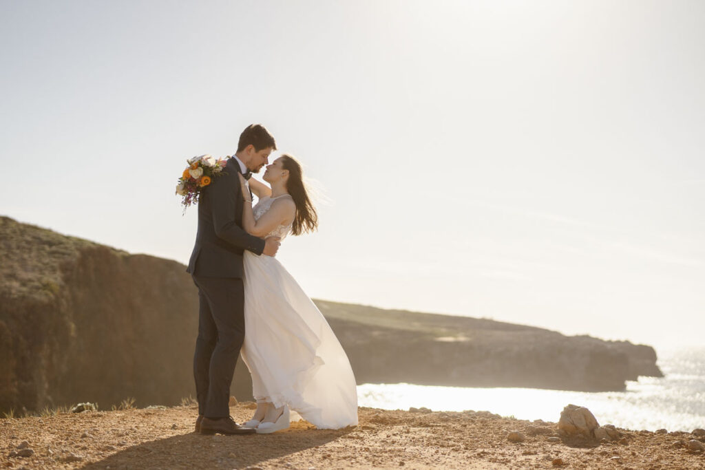 Bride and groom embraced at cliff in Bordeira, Portugal