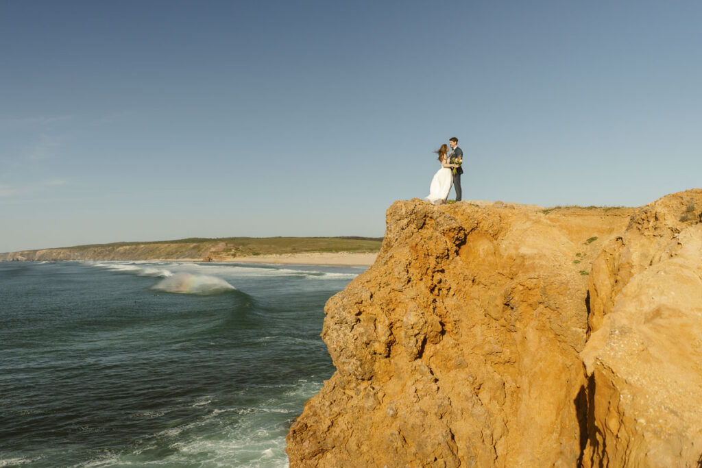 Bride and groom at cliff edge in Bordeira, Portugal