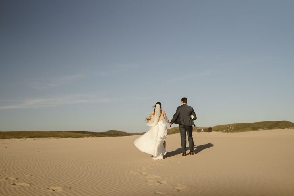 Bride and groom walk on beach in Bordeira, Portugal