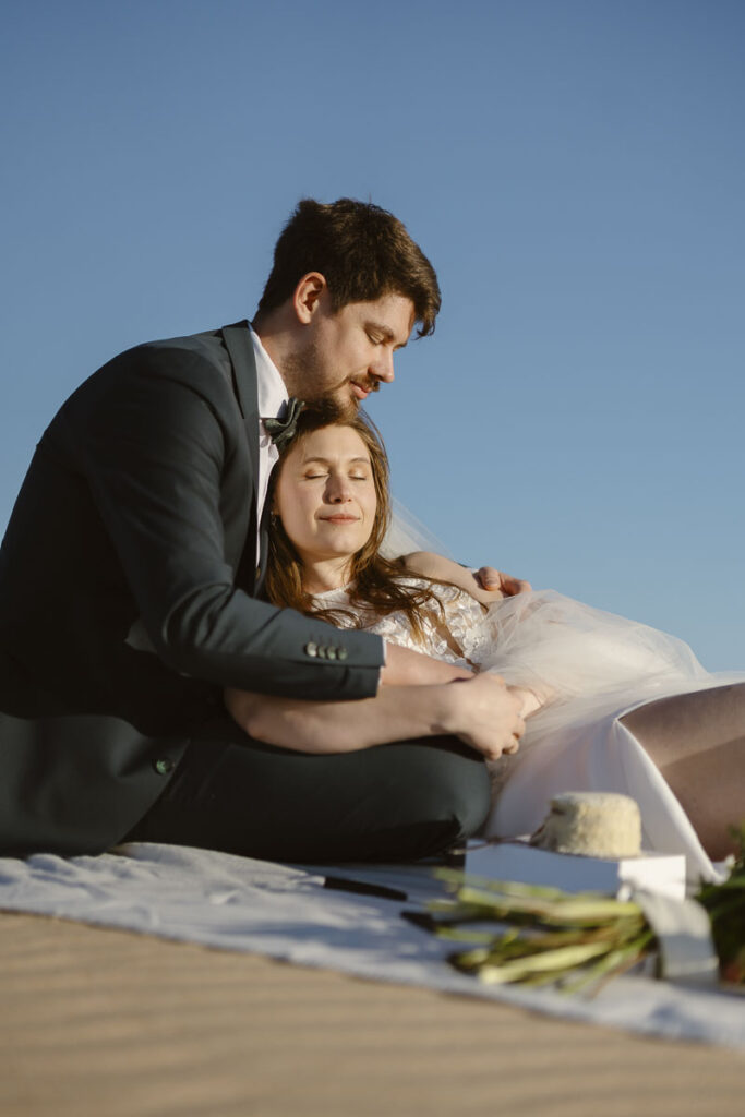 Bride and groom sat on beach in Bordeira, Portugal