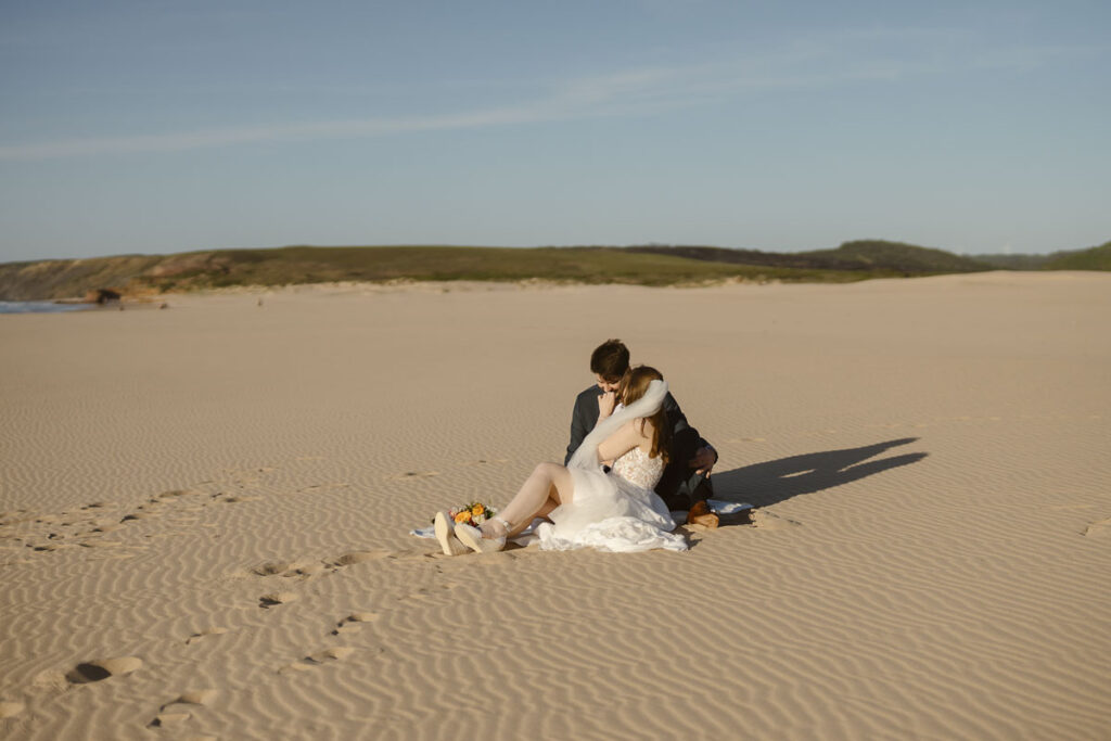 Bride and groom sat on beach in Bordeira, Portugal