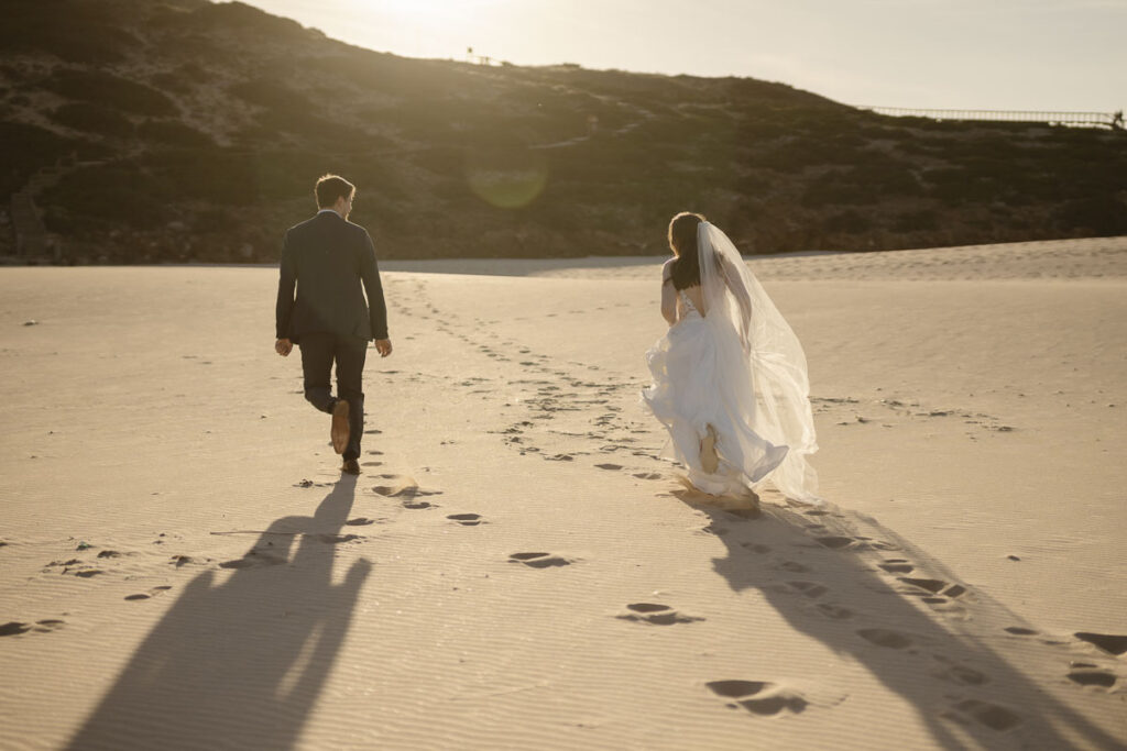 Bride and groom walk on beach in Bordeira, Portugal