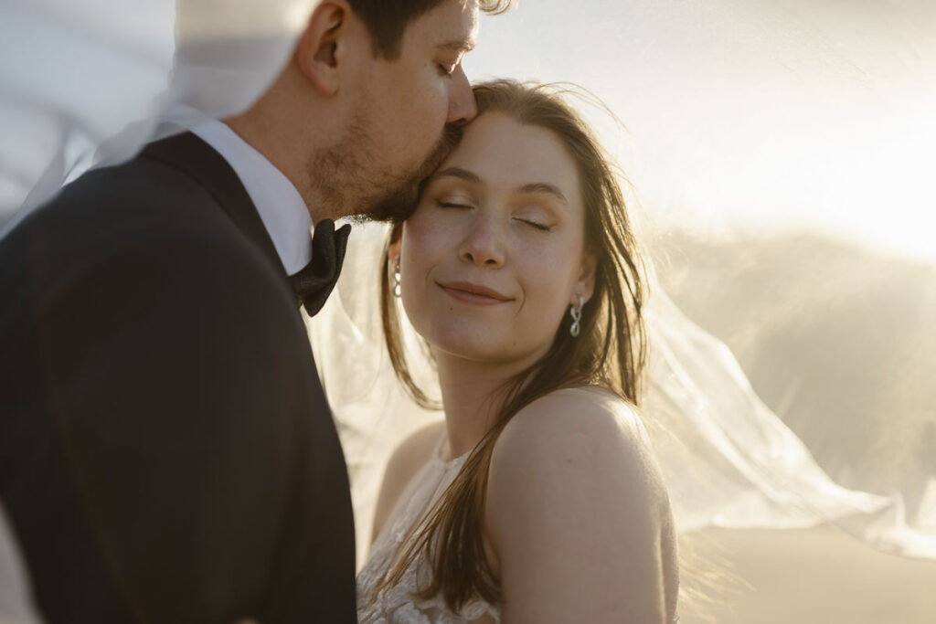 Groom kisses brides forehead in Bordeira, Portugal