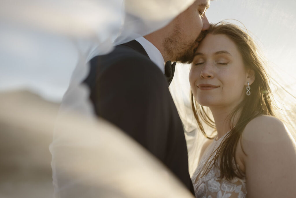 Groom kisses bride on forehead in Bordeira, Portugal