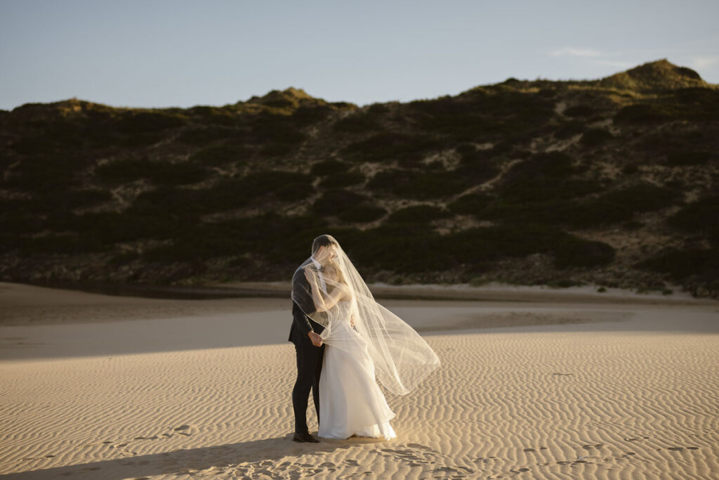 Bride and groom under veil in Bordeira, Portugal