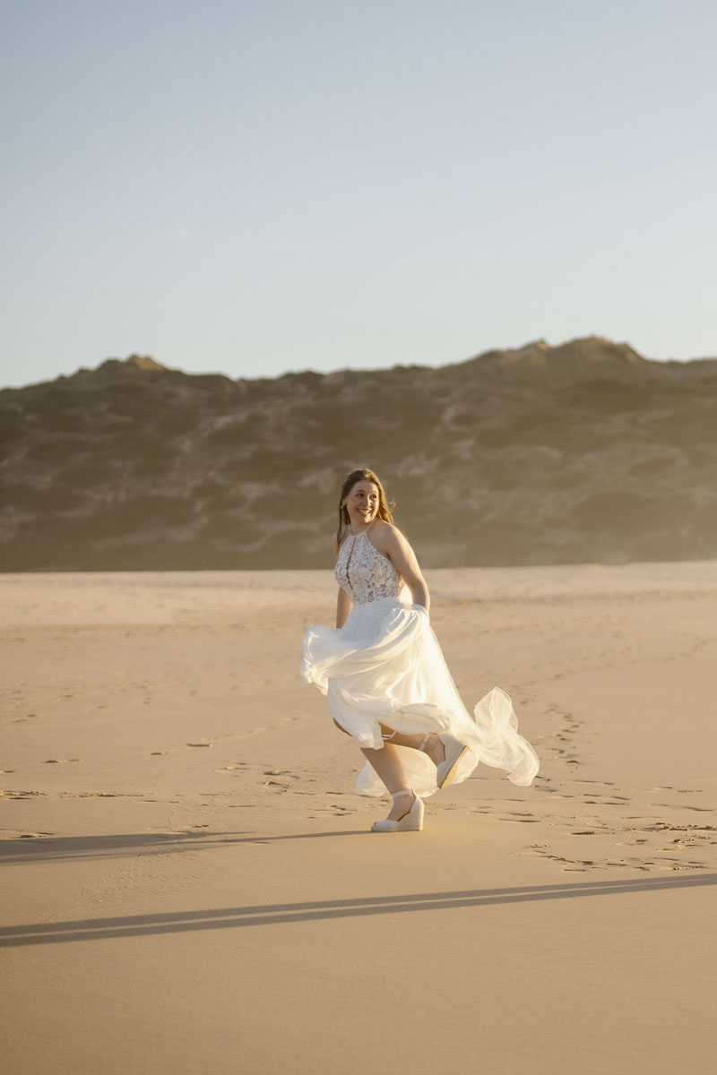 Bride runs on beach in Bordeira, Portugal
