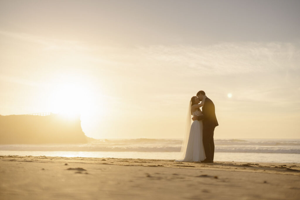 Bride and groom kiss on beach in Bordeira, Portugal