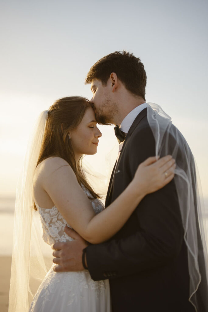 Groom kisses bride's forehead in Bordeira, Portugal