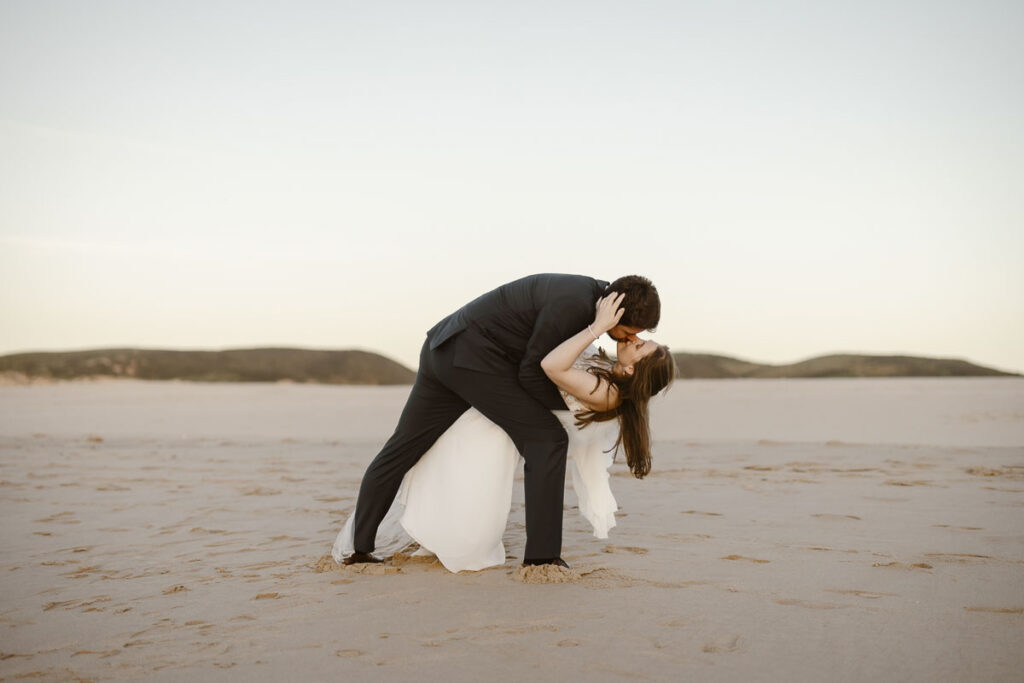 Groom kisses bride on beach in Bordeira, Portugal