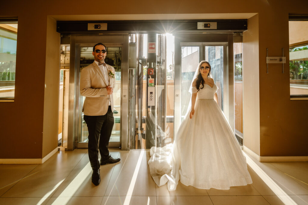 A wife and groom wearing sunglasses in front of a hotel entrance